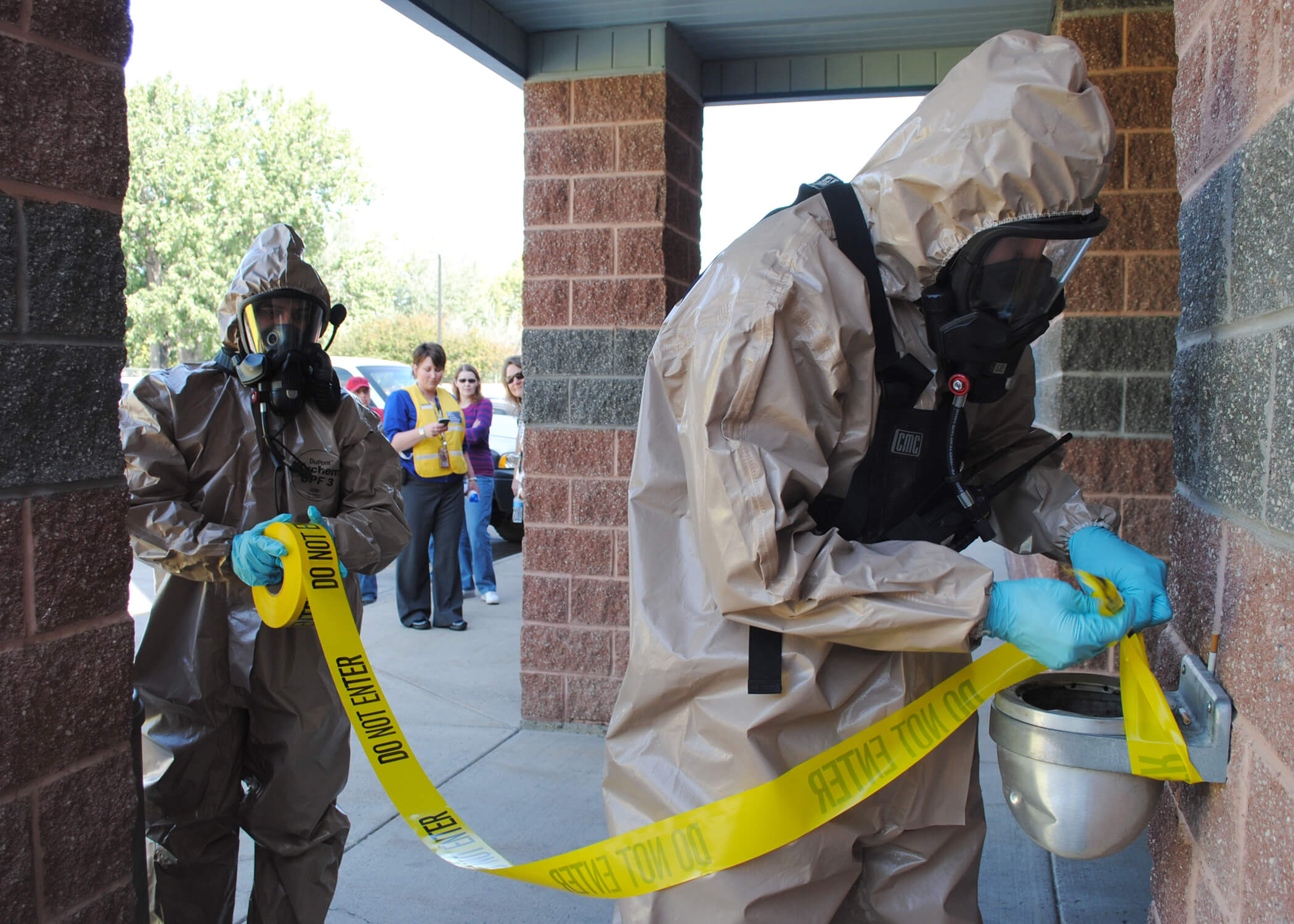 Emergency personnel in protective gear stringing up yellow tape 