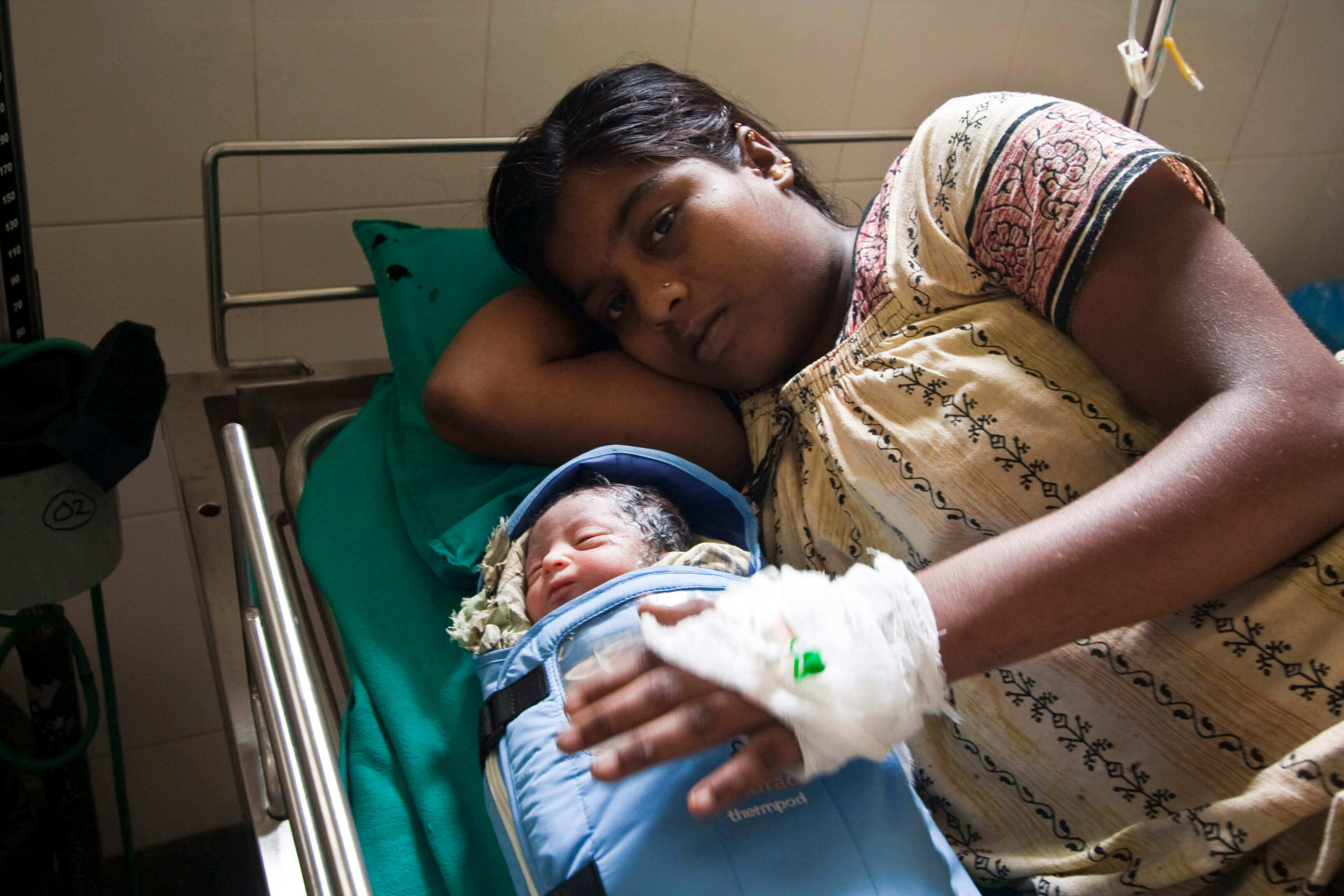 Mother lying in bed with her newborn infant, who is covered by blankets infused with NASA technology