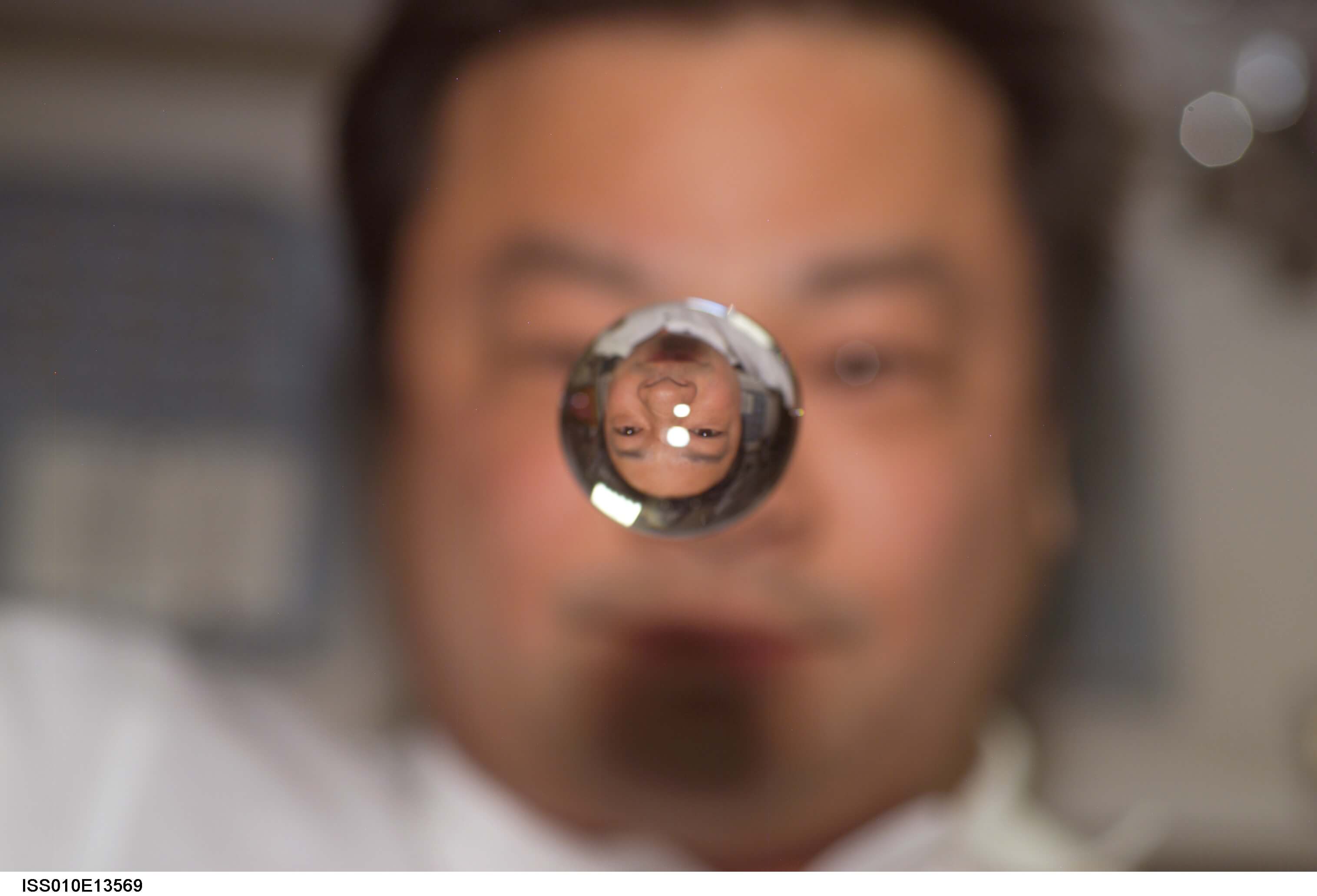 The image of an astronaut's face is inverted through a floating drop of water 
