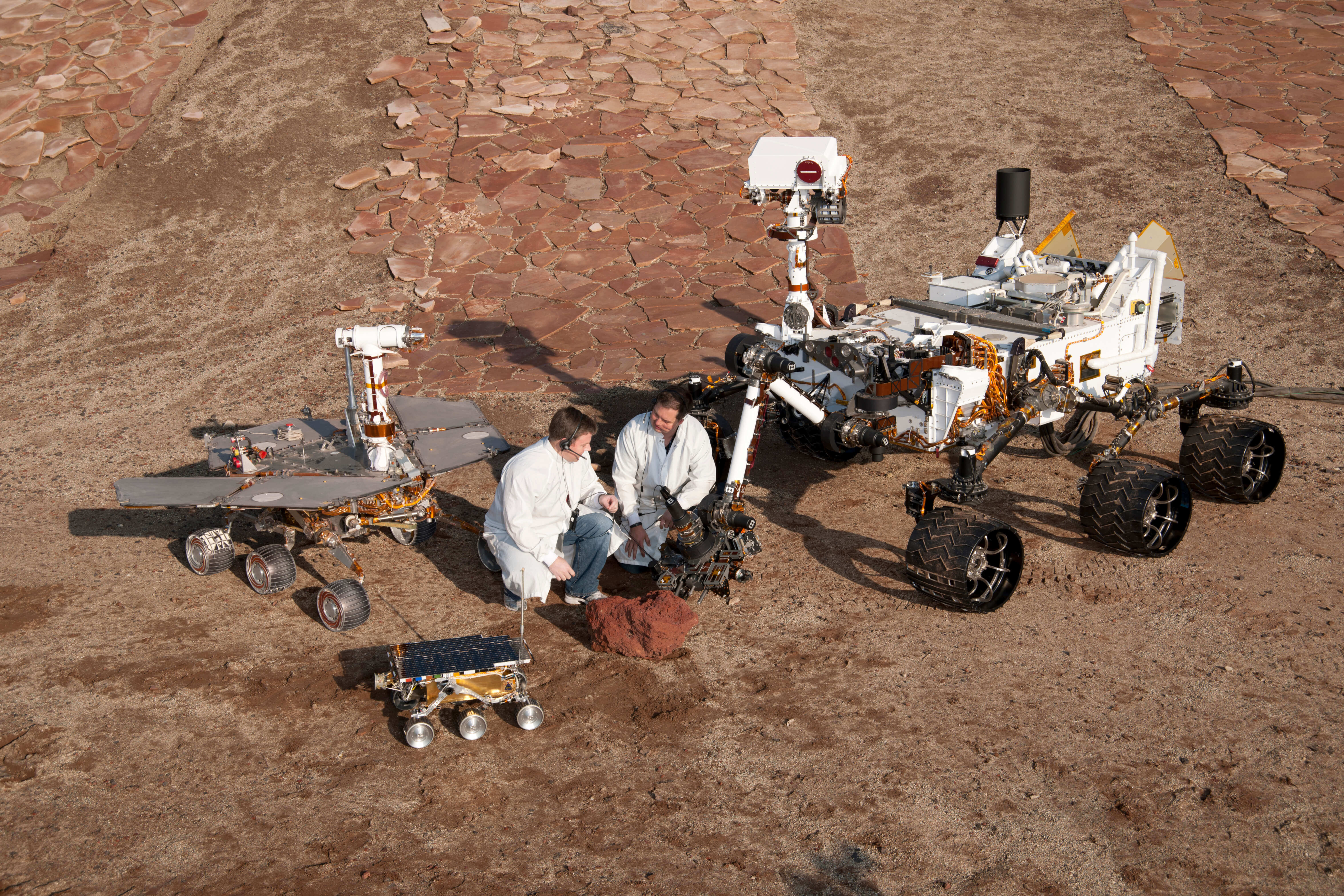 Two spacecraft engineers with models of three generations of Mars rovers 