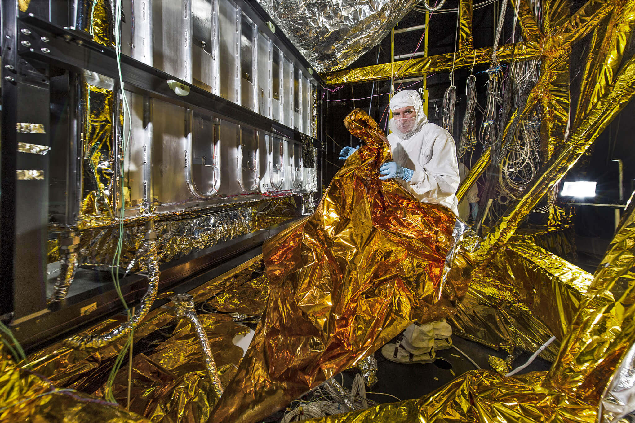 Engineer lays radiant barrier insulation over wires on floor of NASA's Space Environment Simulator 