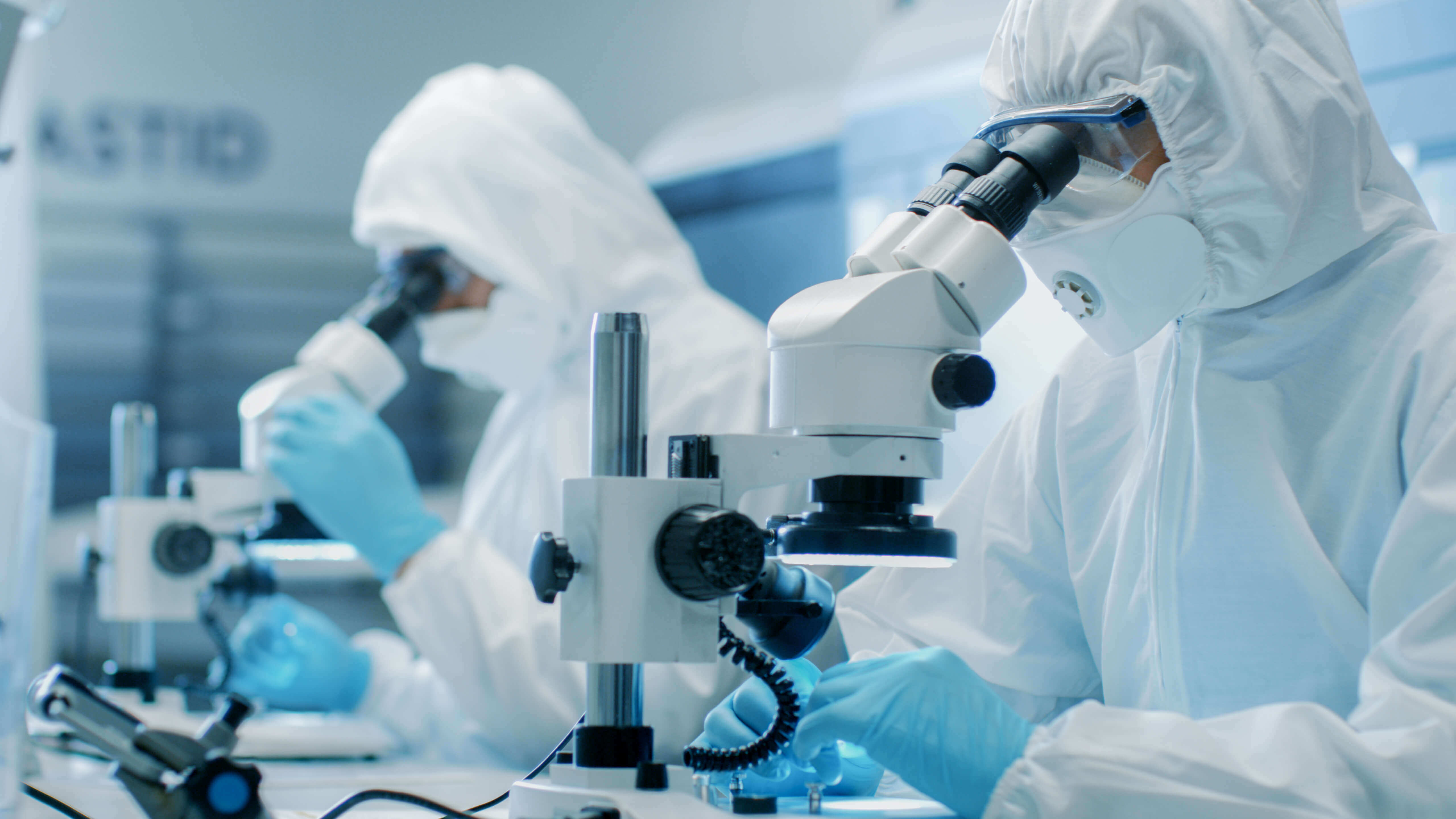 Researchers in clean room garments use microscopes in a laboratory 