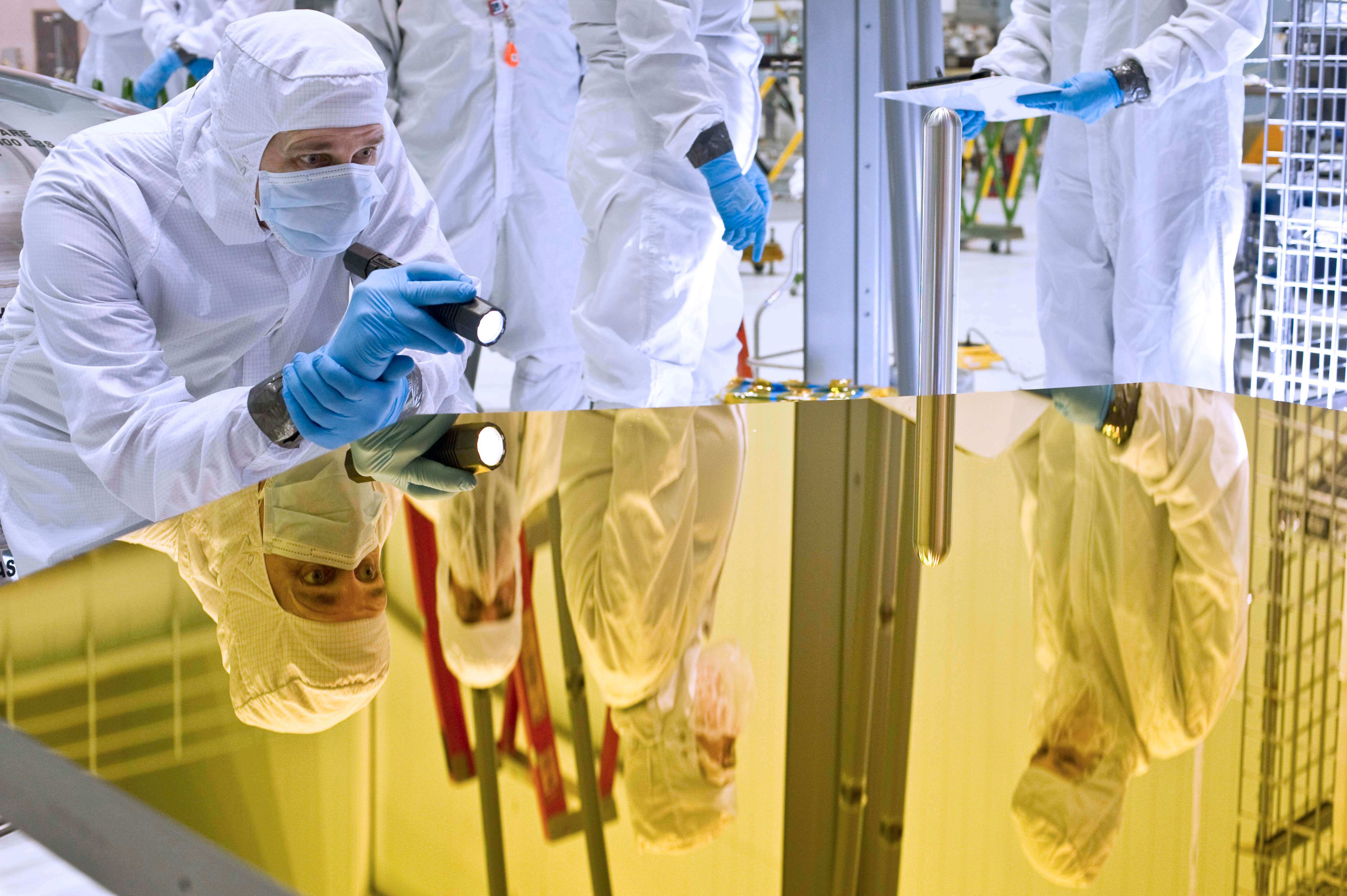 NASA engineers in clean room garments inspect a mirror for the James Webb Space Telescope 